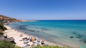 Una playa con agua turquesa cristalina, una orilla de arena y algunas sombrillas y sillas de playa.