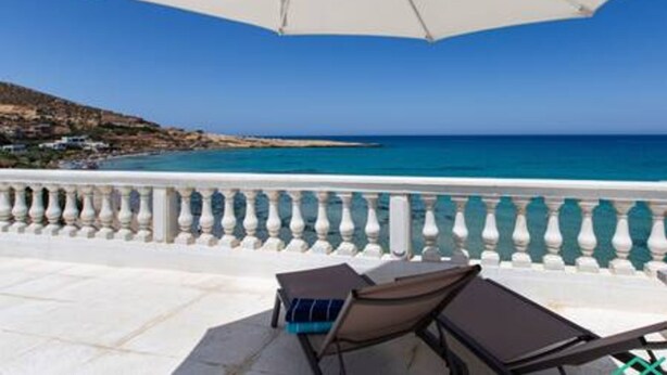 Un balcón con barandilla blanca, una sombrilla y dos sillones de relax frente a una vista costera.
