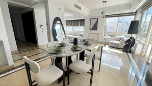 A modern dining area with a marble table, white cushioned chairs, and a view of the city through large windows. - Black & White: Modern & Spacious (Tunis)