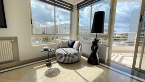 A modern room with a large bay window, a round ottoman, a small table with a decorative item, and a black lamp. - Black & White: Modern & Spacious (Tunis)