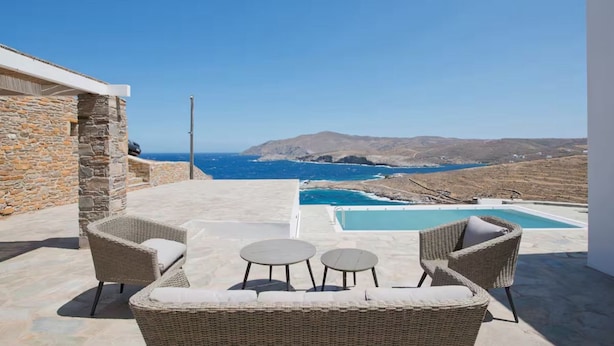 Área de piscina com móveis de vime e vista para o mar e montanhas.