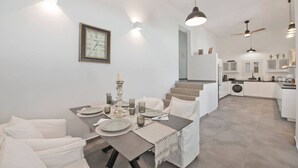 Uma área de jantar moderna com uma mesa posta para quatro pessoas, um relógio na parede e uma escada que leva a uma cozinha.
