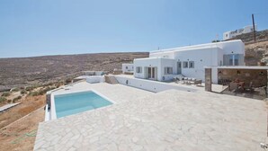 Uma villa branca moderna com piscina e área de estar ao ar livre, com vista para uma paisagem acidentada.