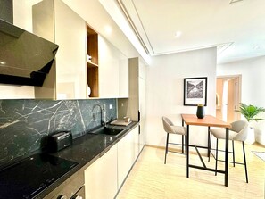 A modern kitchen with a black marble countertop, a built-in oven, and a dining area with two chairs and a table. - Superbe logement luxueux à JDC (Carthage)