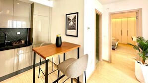 Una cucina moderna con un piano di lavoro in marmo, un tavolo da pranzo con due sedie, un quadro appeso al muro e una pianta in vaso nell'angolo.