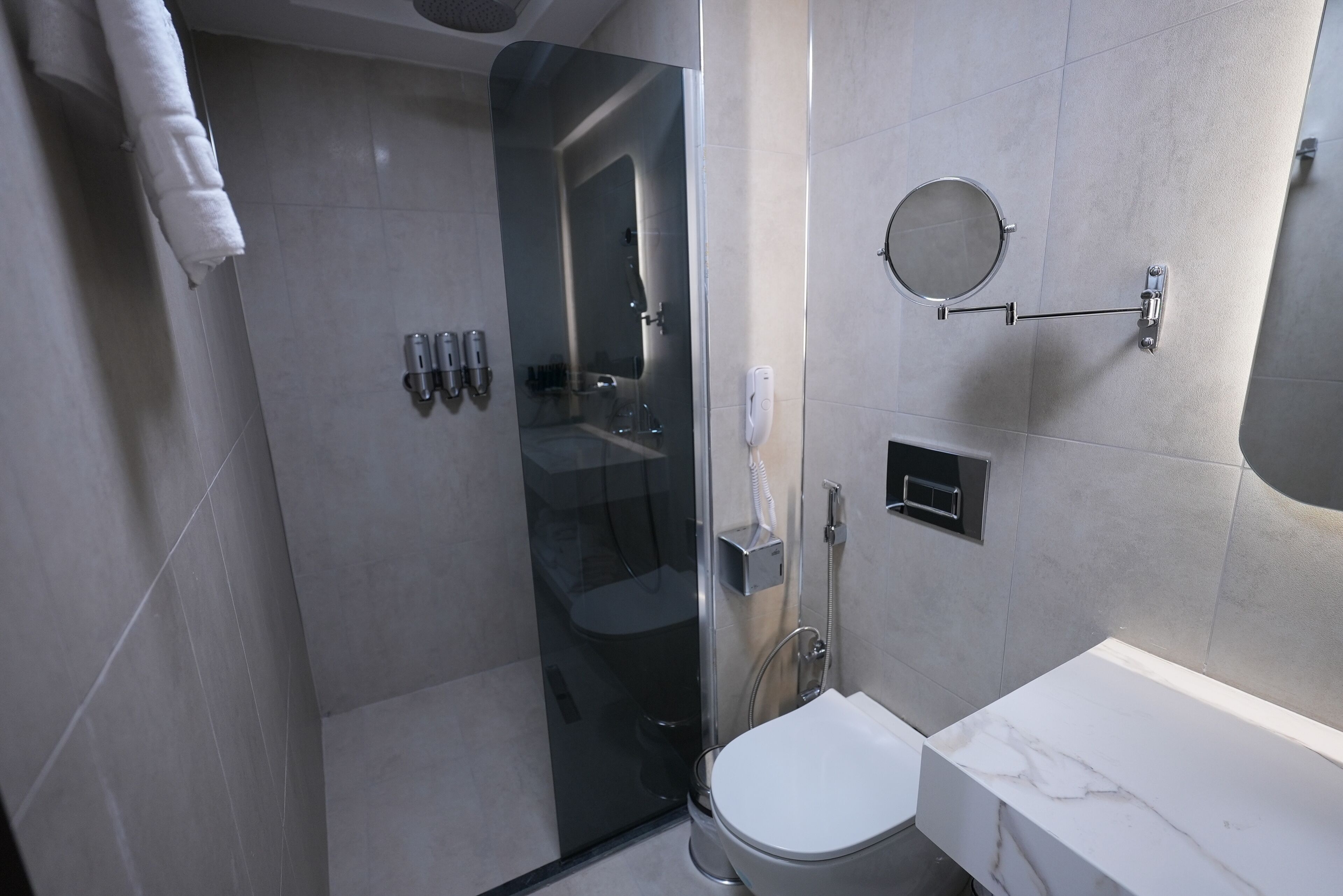 Un baño moderno con ducha envuelta en vidrio, inodoro blanco y encimera de mármol.