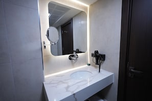 A modern bathroom with a white marble sink, a round mirror, and a dark wooden door. - THE NAVA HOTEL (Van)