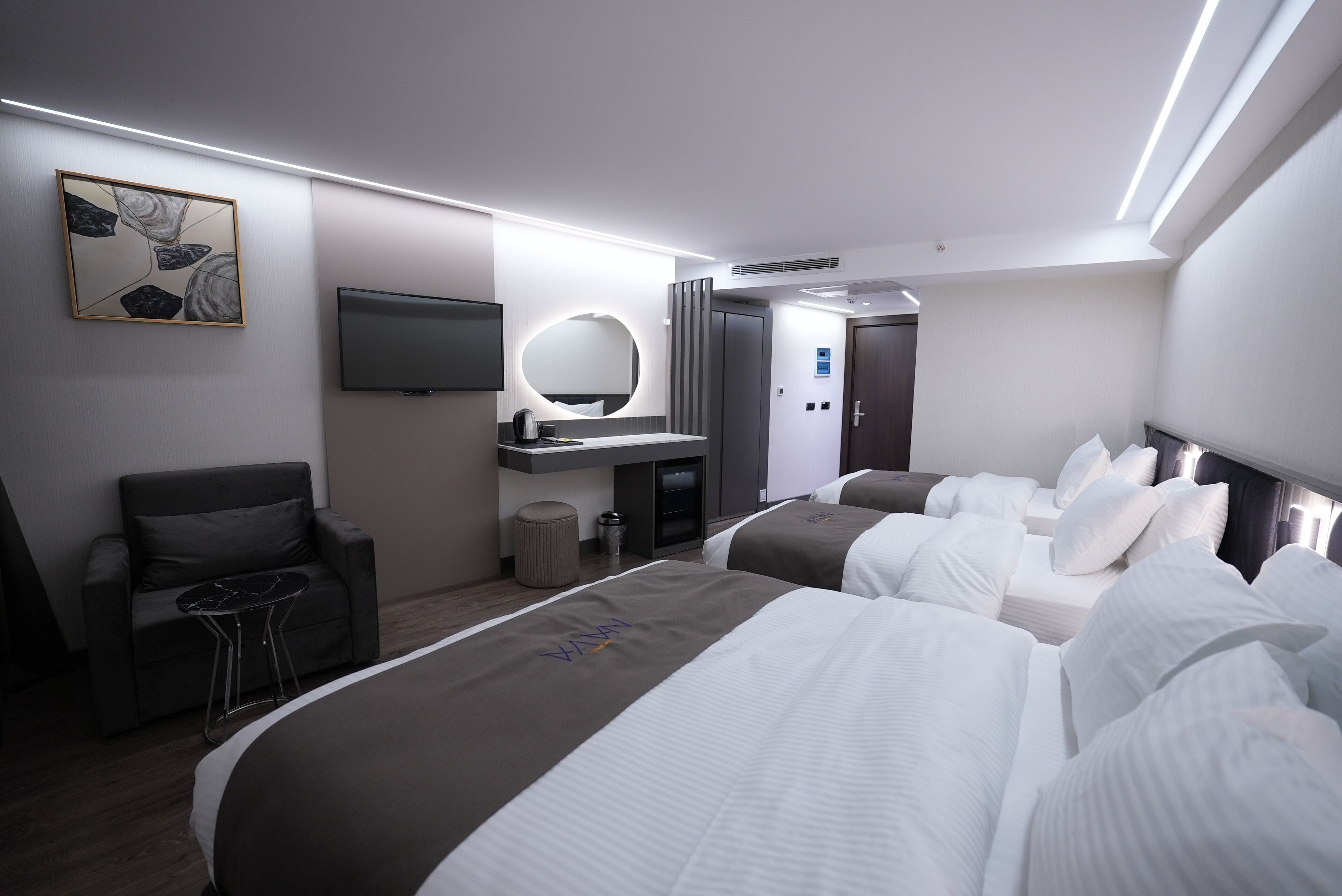 A modern hotel room with two beds, a flat-screen TV, a round mirror, a sofa, and a small table.