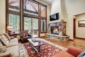 A cozy living room with a fireplace, large windows, and a television. - Belemere Lodge in Blue River (Blue River)