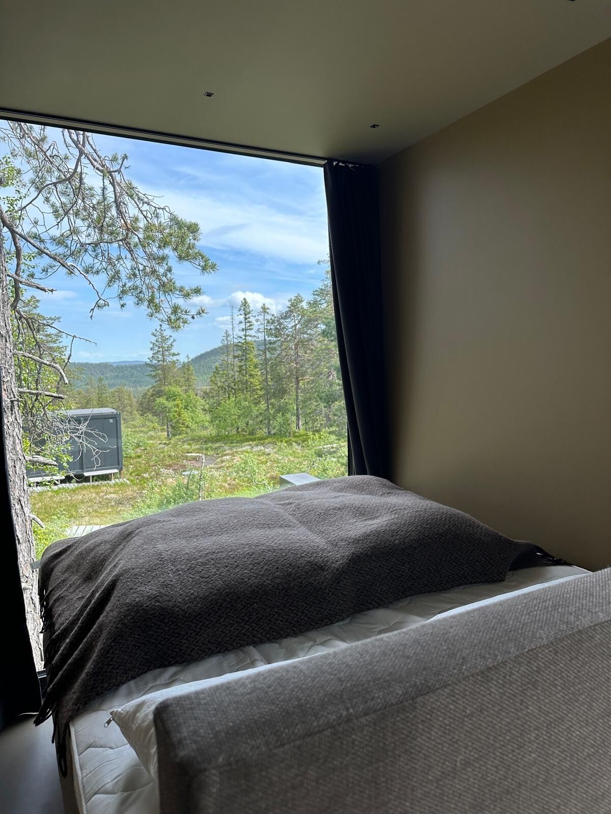 A bedroom with a bed, a window, and a view of a forested area.