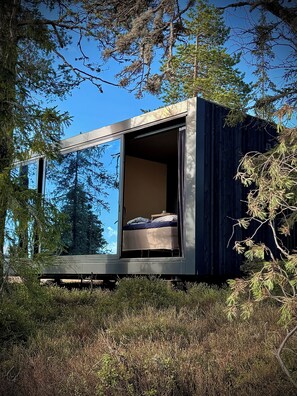 A modern, minimalist cabin with a bed and a small table, surrounded by dense forest. - Unique, Modern Cabin at Blefjell (Flesberg)