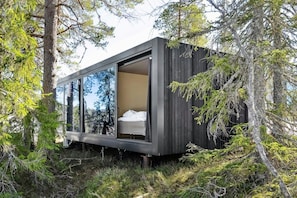 A modern cabin with a glass wall, a bed, and a forested backdrop. - Unique, Modern Cabin at Blefjell (Flesberg)
