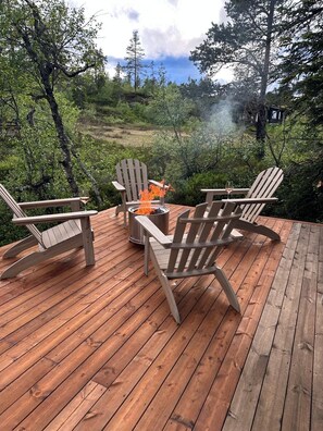 A wooden deck with Adirondack chairs and a fire pit.