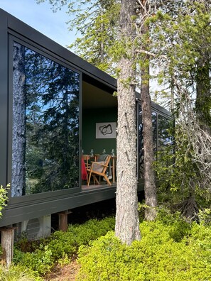 A modern building with large windows, a dining area with chairs and a table, and a view of surrounding trees.