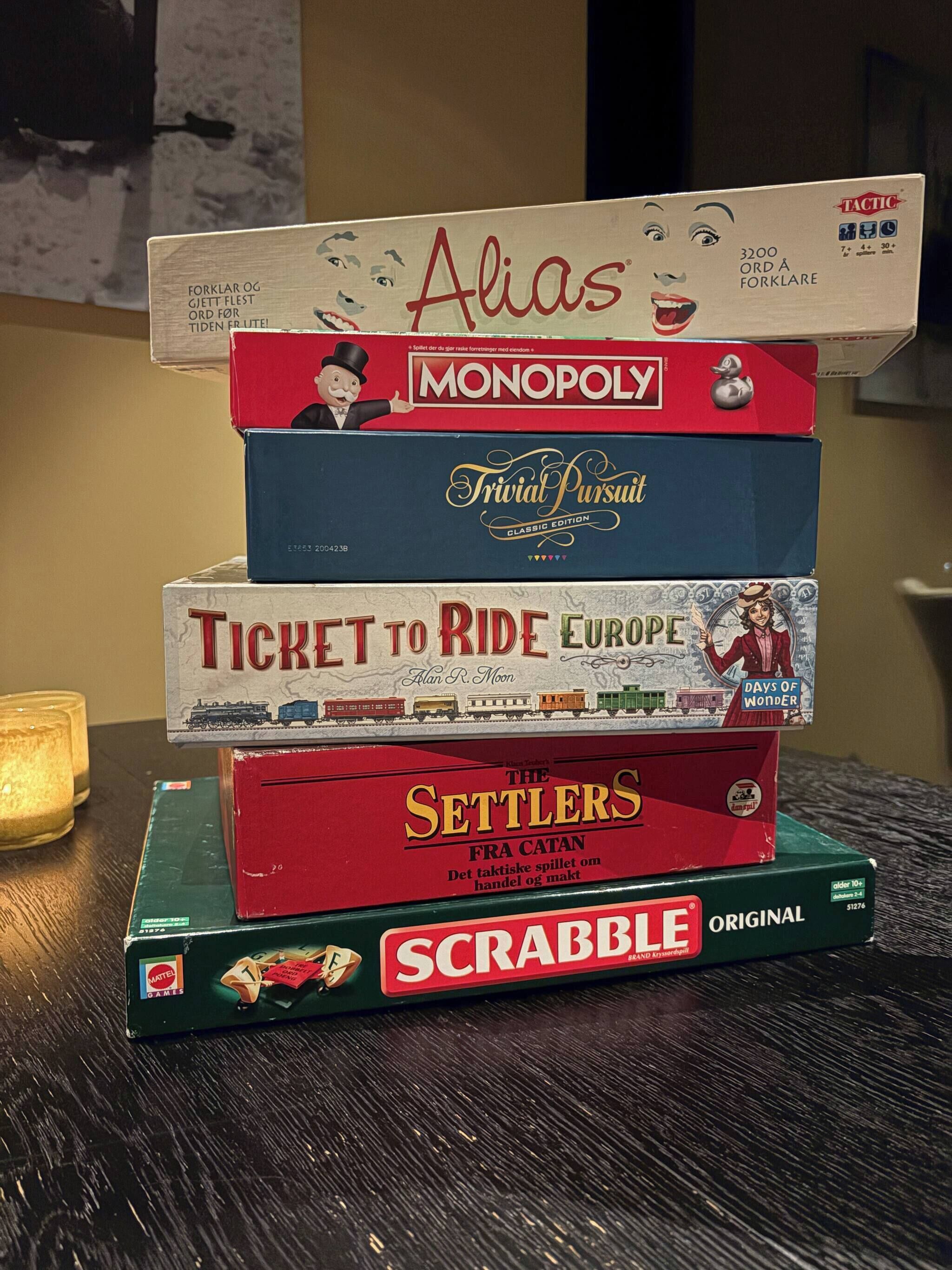 Una pila de juegos de mesa, incluyendo Monopoly, Trivia Pursuit, Ticket to Ride Europa, Los Colonos y Scrabble.
