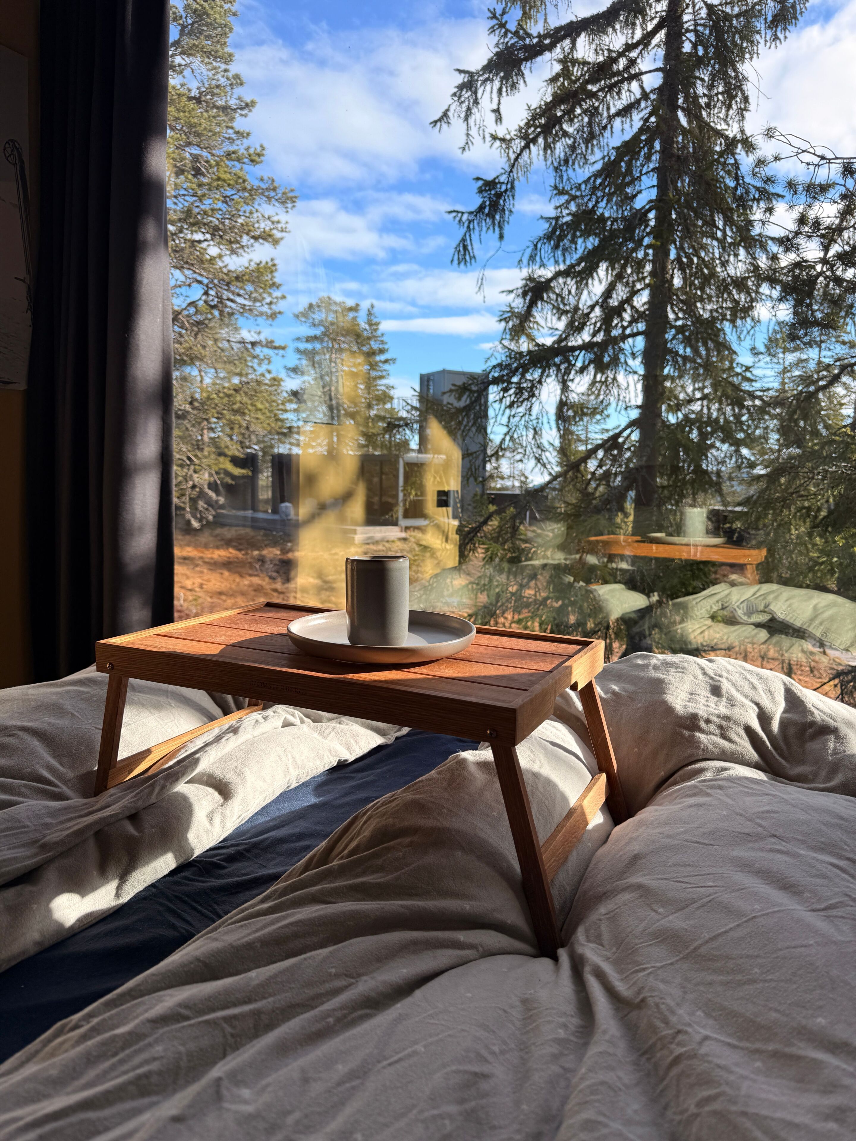 Un lit avec une table en bois et une tasse, le tout mis en valeur par un décor de arbres et un ciel dégagé.