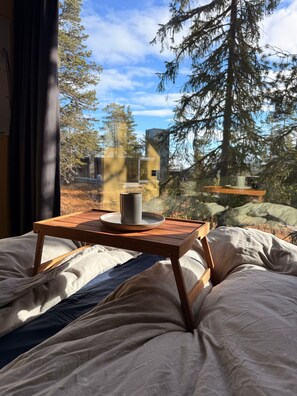 A bed with a wooden table and a cup, set against a backdrop of trees and a clear sky. - Unique, Modern Cabin at Blefjell (Flesberg)