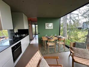 A modern kitchen with a dining area, a view of trees, and a bench.