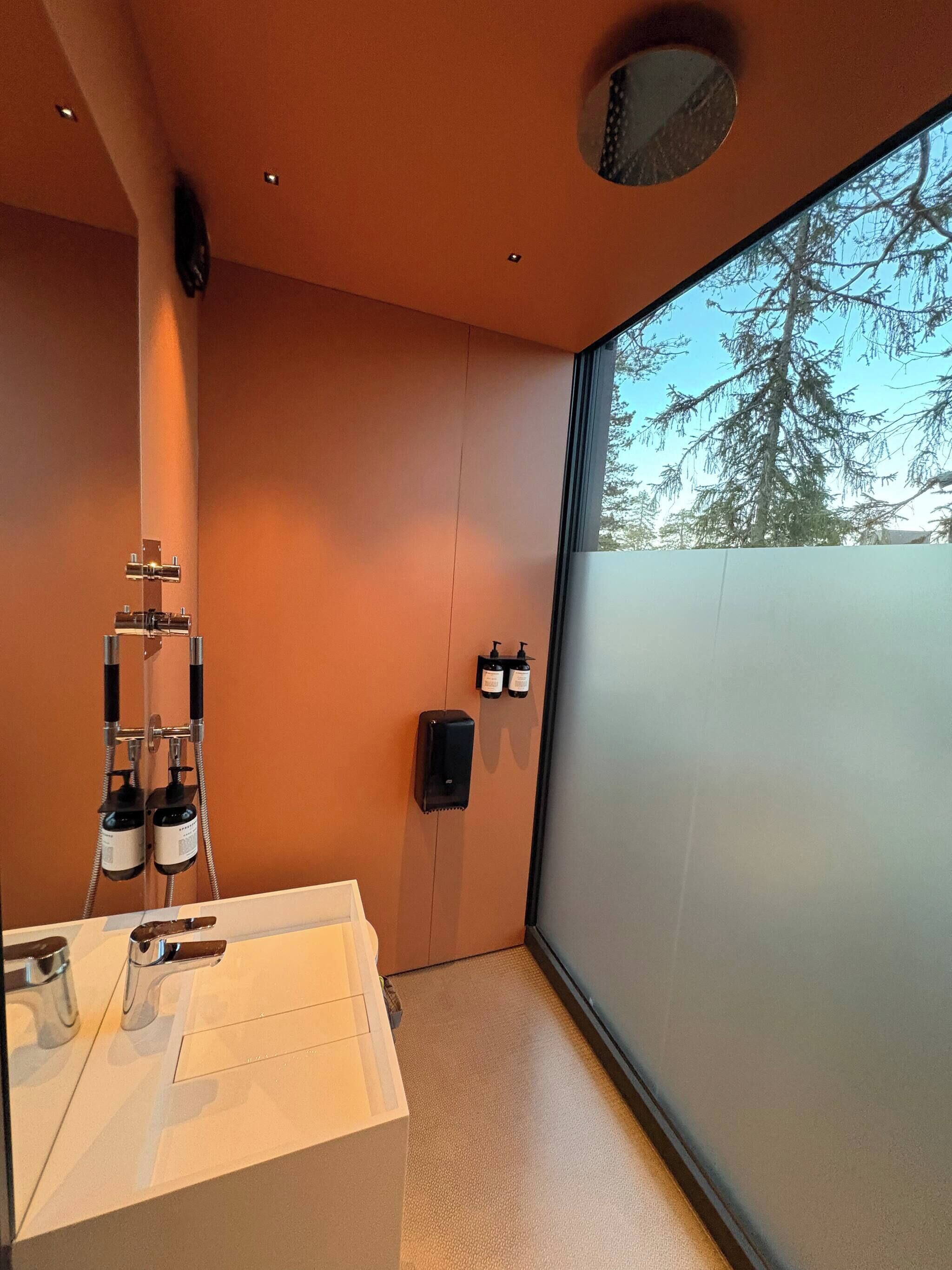Ein modernes Badezimmer mit großem Fenster, einer Dusche und einem Waschbecken.