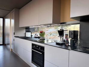 A modern kitchen with a large island, built-in oven, and a coffee maker.