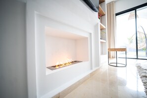 A modern living room with a built-in fireplace, a large window, and a wicker chair. - Modernity Villa exceptionnelle à Hammamet Centre (Hammamet Sud)