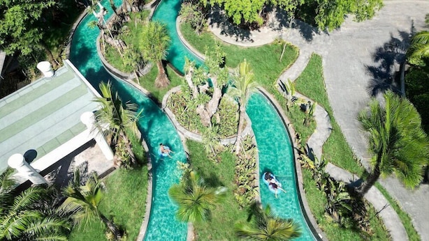 Luftaufnahme eines Resorts mit einem gewundenen Pool, umgeben von üppiger Vegetation und Palmen.
