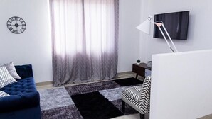 Ein modernes Wohnzimmer mit einem blauen Sofa, einem gemusterten Teppich, einem Fernseher und einer Wanduhr.