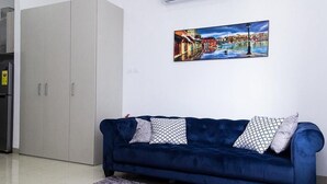 Ein modernes Wohnzimmer mit einem dunkelblauen Sofa, zwei gemusterten Kissen, einem großen Gemälde einer europäischen Kanalansicht und einem weißen Kleiderschrank.