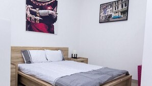 Ein Schlafzimmer mit einem hölzernen Bett, weißer Bettwäsche und zwei an der Wand befestigten Kunstwerken.