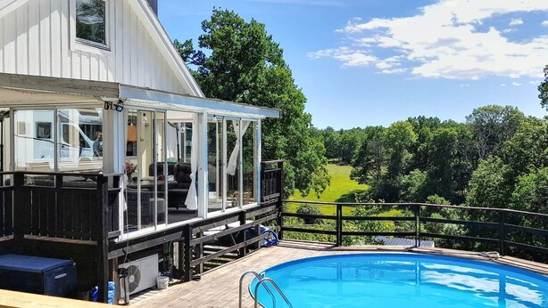 A pool area with a wooden deck, a covered seating area, and a view of a green landscape. - 4 Star Holiday Home in Ingaro (Värmdö)