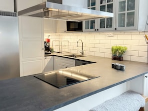 Cozinha moderna com micro-ondas embutido, pia de aço inoxidável e fogão por indução preto.