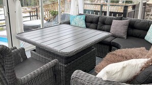 A covered outdoor seating area with a table and wicker furniture, overlooking a wooden deck and a pool. - 4 Star Holiday Home in Ingaro (Värmdö)