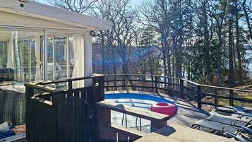 Um deck moderno ao ar livre com estrutura de vidro, piscina e vista para uma área arborizada.