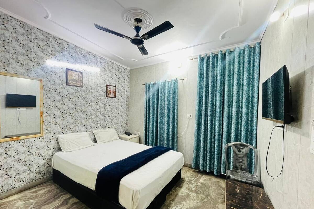 A bedroom with a bed, a ceiling fan, a TV, and curtains.