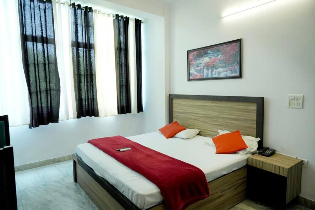 A hotel room with a bed, a nightstand, a telephone, a painting on the wall, and a window with curtains.