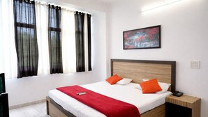 Una habitación de hotel con cama, mesita de noche, un cuadro y una ventana con cortinas.