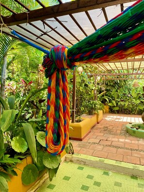 A hammock tied to a wooden structure in a garden with potted plants and a tiled floor.