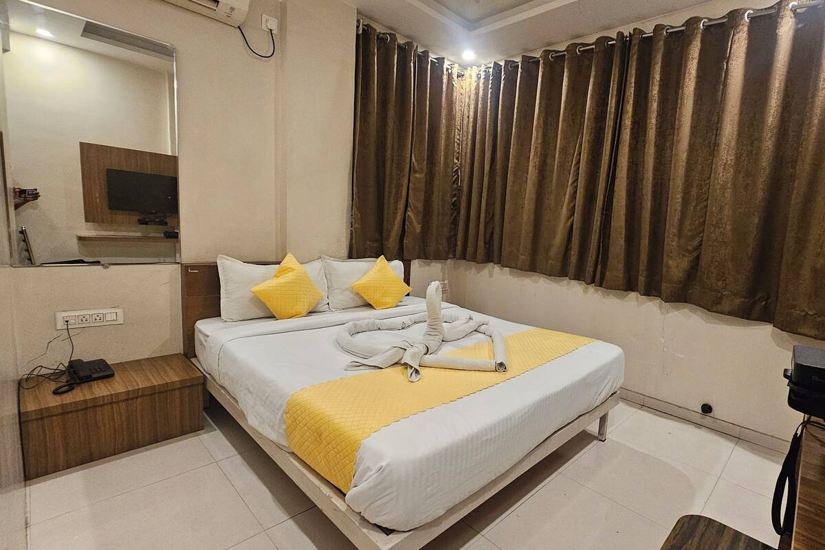 A hotel room with a bed, a bedside table, a mirror, a TV, and curtains.
