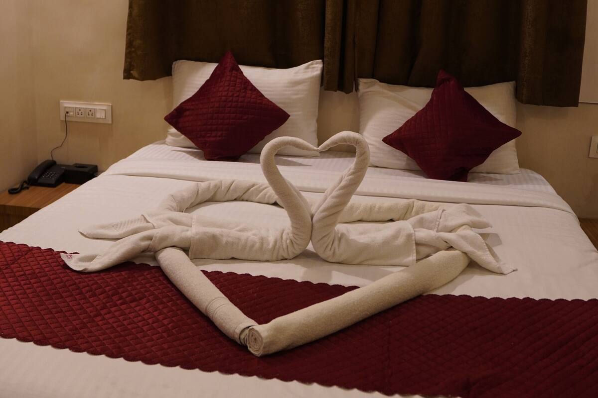 A hotel room with a neatly made bed, two pillows, a telephone, and a power outlet on the wall.