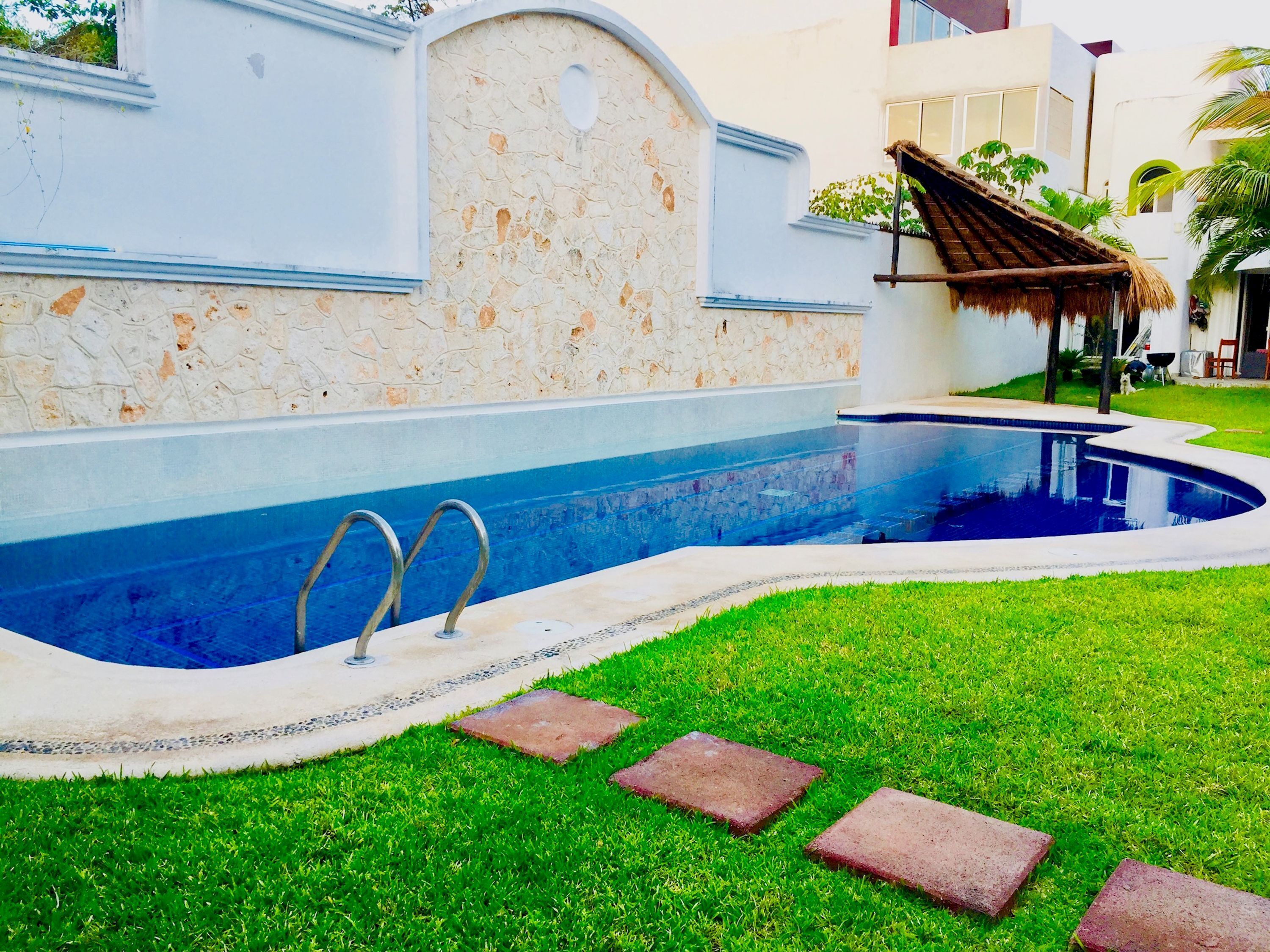 Una piscina con un muro in pietra e una struttura a tetto di paglia.