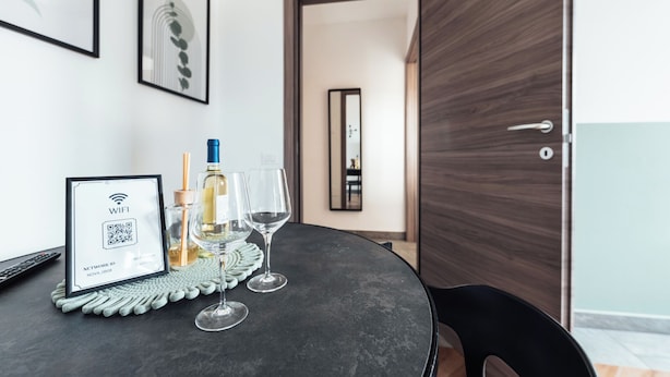 Een moderne kamer met een ronde tafel, twee wijnglazen, een fles wijn, een bord met daarop het WiFi-symbool, en een deur die naar een andere kamer leidt.