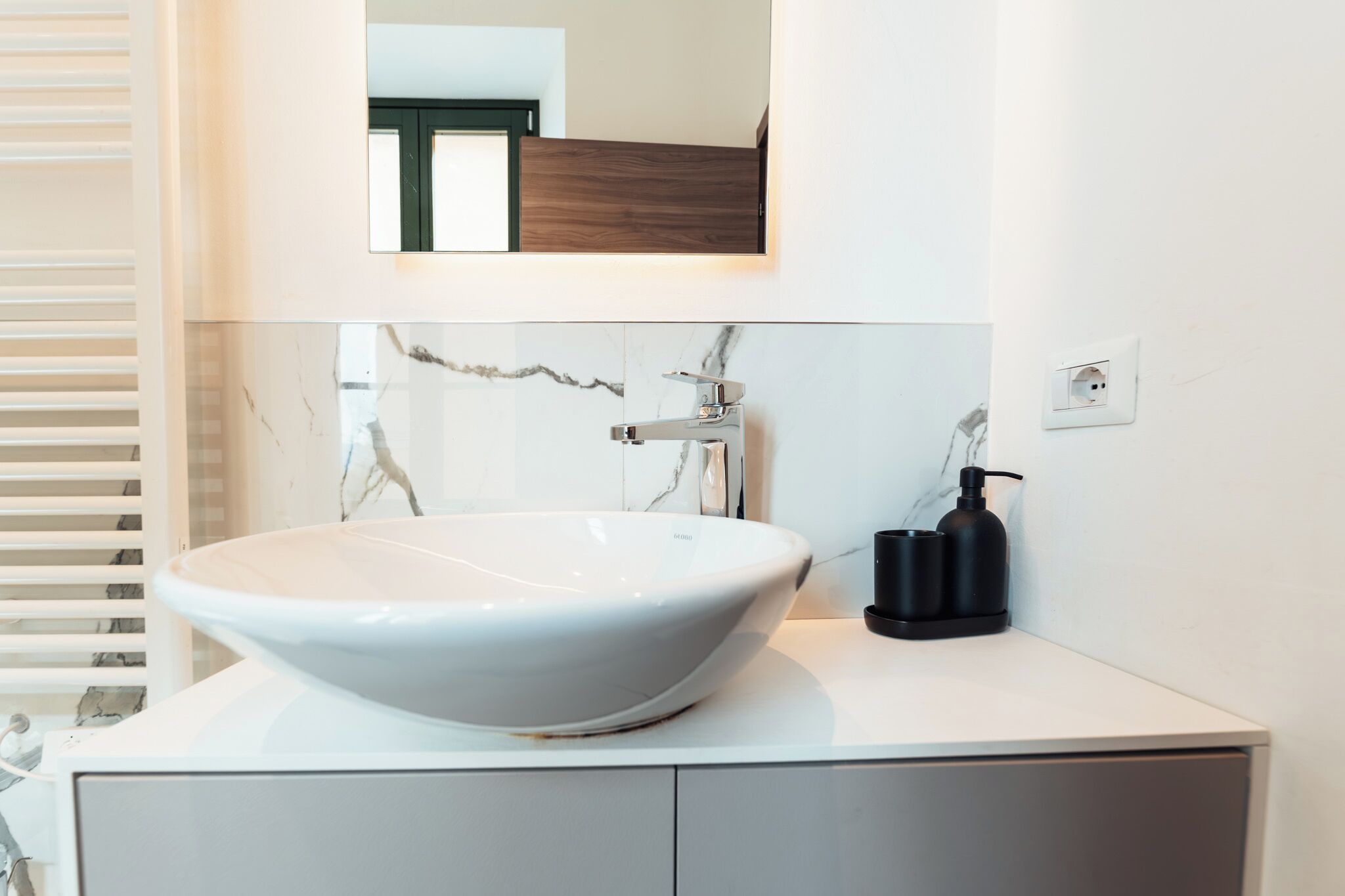 Une salle de bain moderne avec un grand lavabo blanc sur pied, un miroir au-dessus et un distributeur de savon noir posé sur le comptoir.