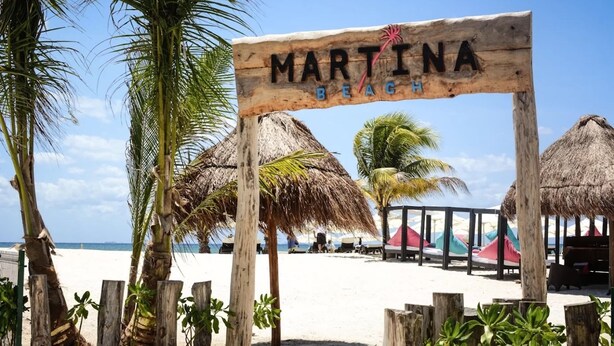 Un panneau en bois portant l’inscription « MARTINA BEACH » et sur lequel on voit un palmier au premier plan.