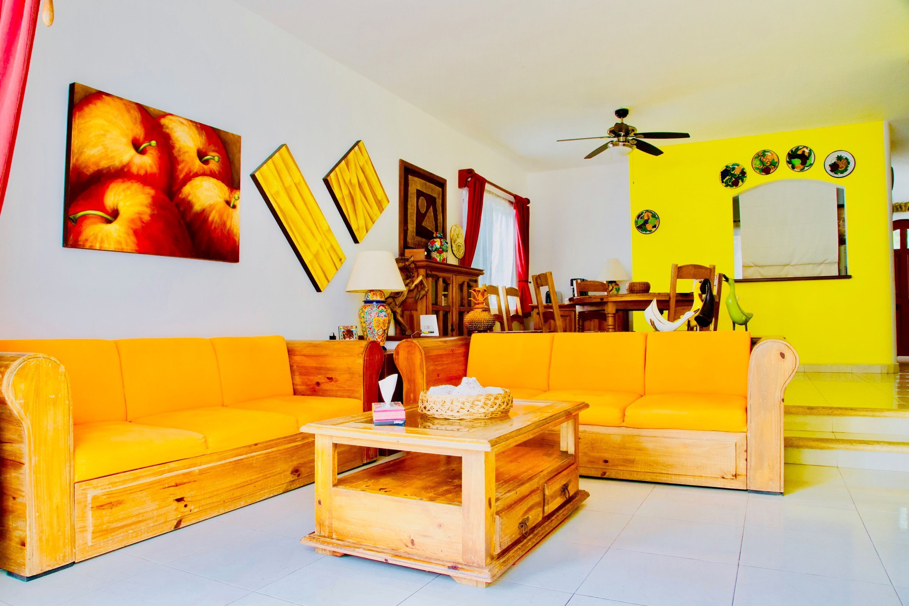 Ein helles Wohnzimmer mit gelben Sofas, Holzmöbeln und einem Deckenventilator.