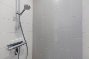 Een douche met een handdouche, een zeepdispenser en een bedieningspaneel aan de muur.