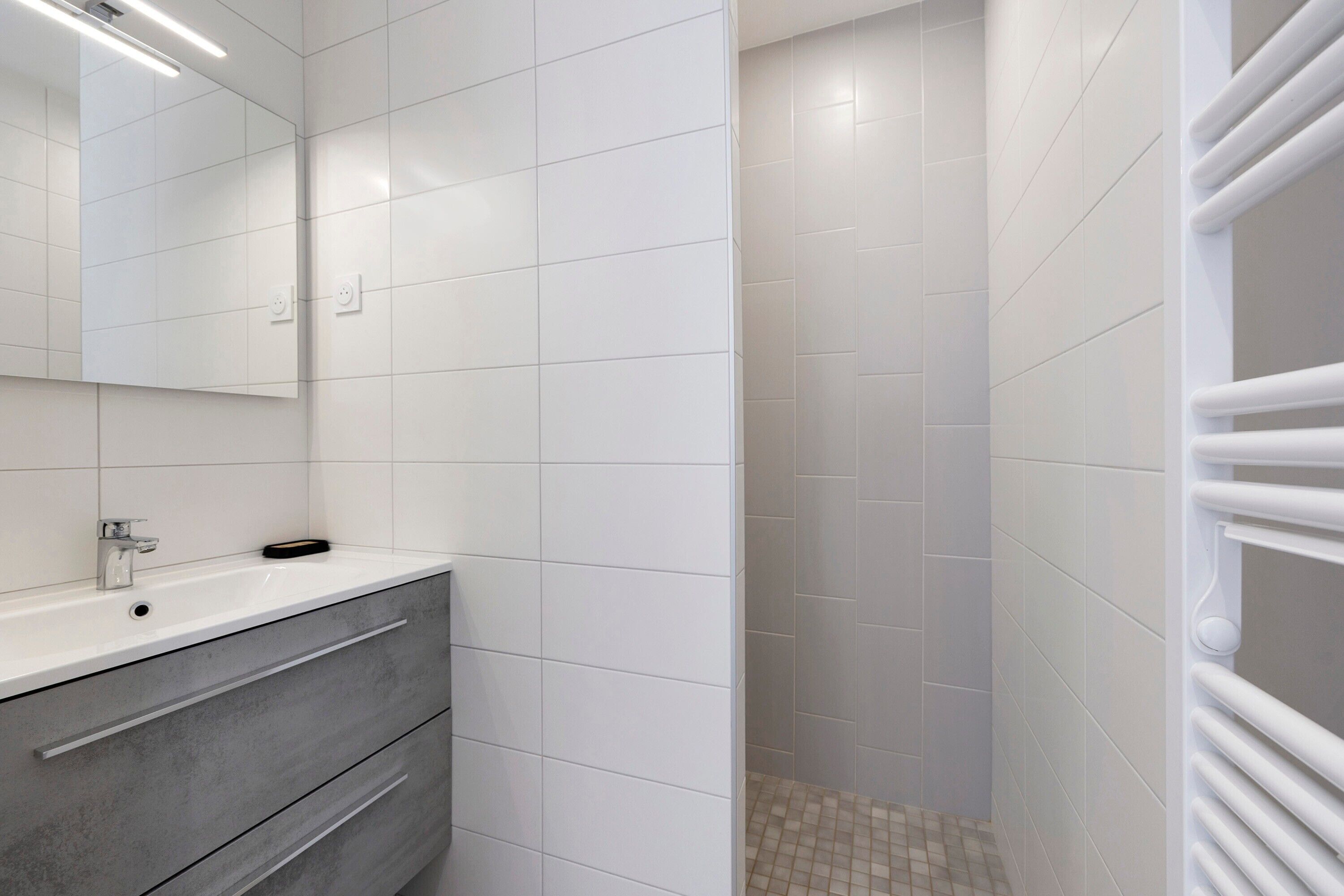 Une salle de bain avec un lavabo blanc, un miroir et des murs carrelés.