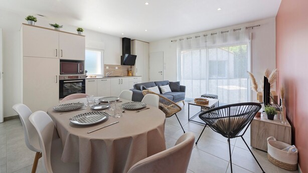 Eine moderne Küche mit integrierten Geräten, ein Essbereich mit rundem Tisch und Stühlen sowie eine Wohnbereich mit einer Couch und Zierpflanzen.