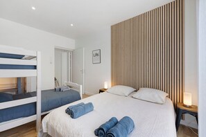 Een slaapkamer met stapelbedden, een groot bed met opgerolde handdoeken, een houten lambrisering en een lijst met een tekst.