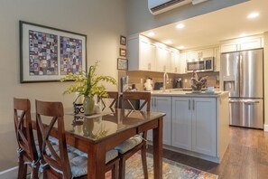 Una cocina moderna con armarios blancos, electrodomésticos de acero inoxidable y un comedor con mesa de vidrio y sillas de madera.