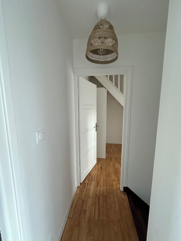 A hallway with wooden flooring, white walls, and a white door leading to a staircase.